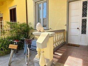 Ein gelbes Gebäude mit einer weißen Tür, einem Balkon mit einem Geländer und einem Fahrrad davor.