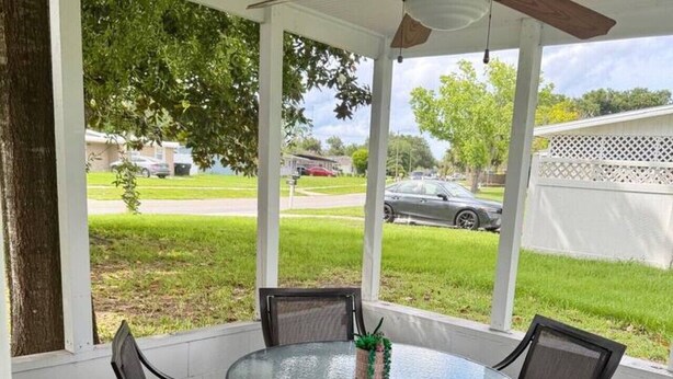 En overdækket terrasse med et rundt bord og stole, en loftsvifte og udsigt til en boligvej.