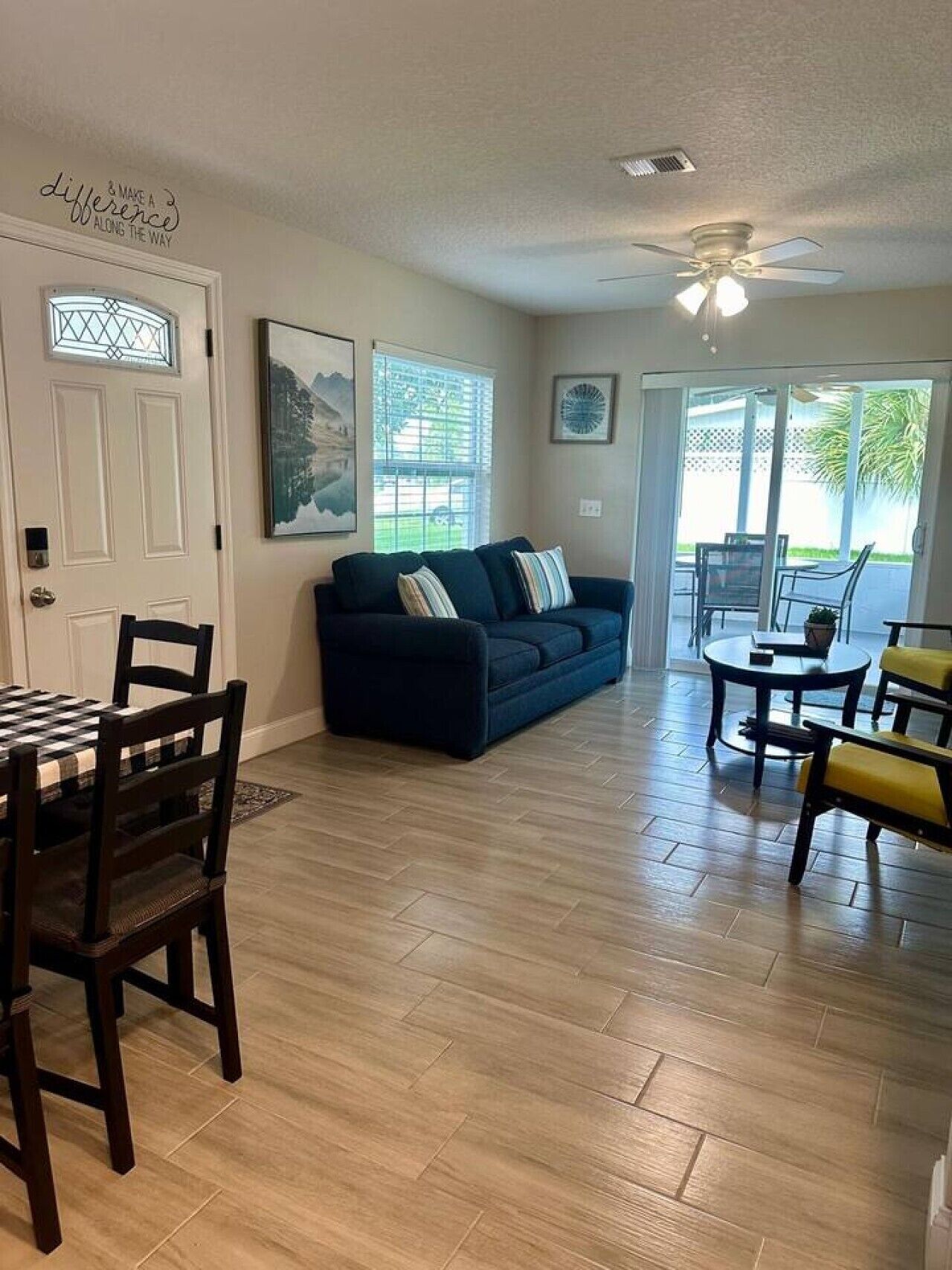 A living room with a dark blue sofa, a dining table with chairs, and a ceiling fan.