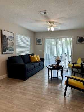A living room with a dark blue sofa, yellow cushions, a round coffee table, and a ceiling fan.