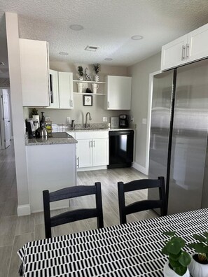 A modern kitchen with white cabinetry, a stainless steel refrigerator, and a dining area with a black and white patterned table.