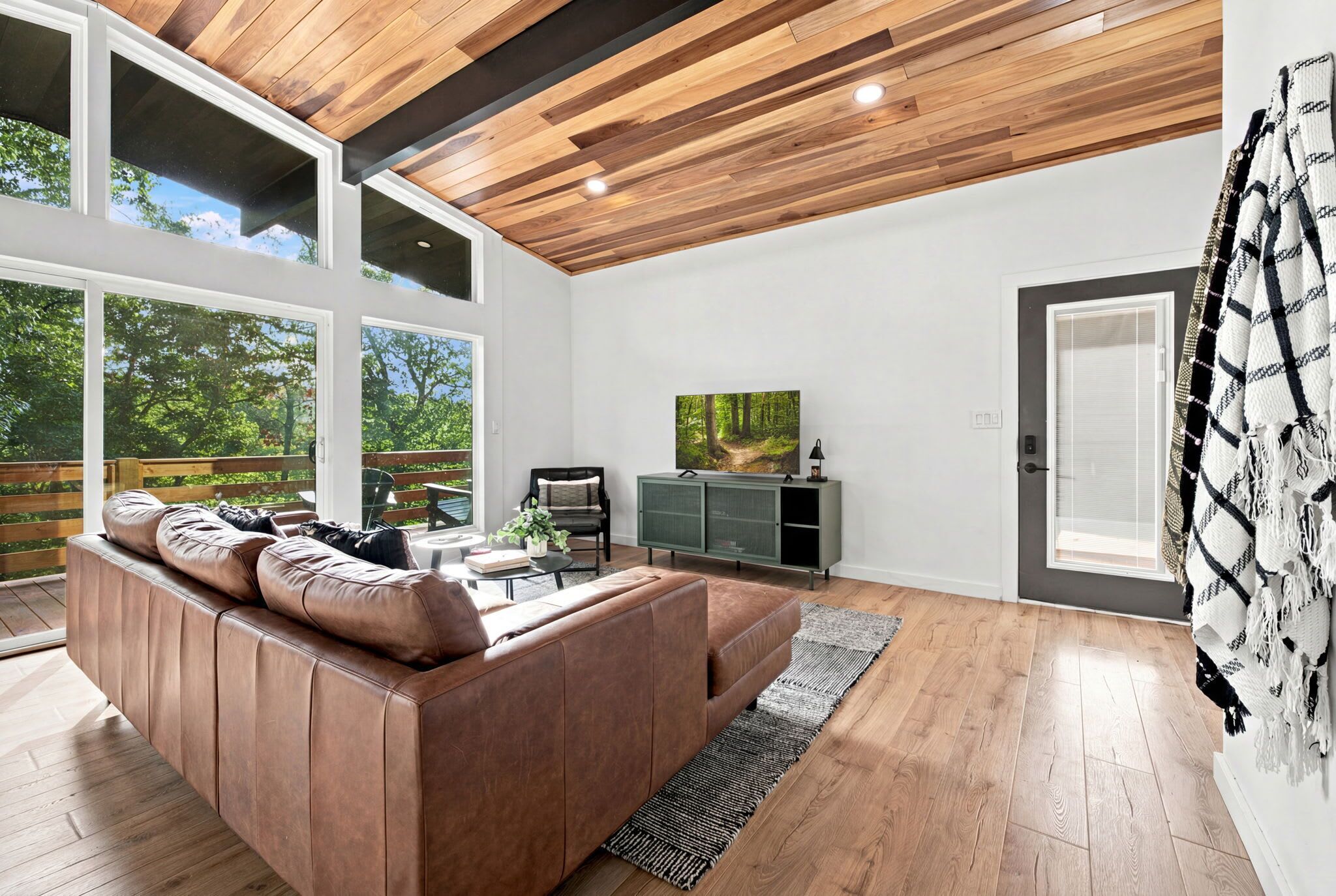 Un salon moderne avec un grand canapé en cuir marron, un téléviseur à écran plat et un plafond en bois.