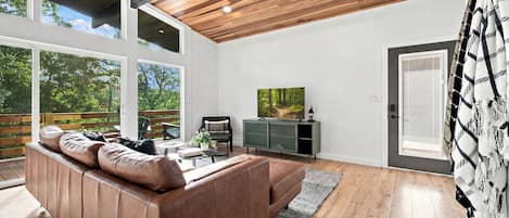 A modern living room with a large brown leather sofa, a flat-screen TV, and a wooden ceiling.