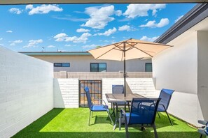 A patio with a table and chairs, a blue umbrella, and a view of a building with windows. - 2BR Scottsdale Ranch Retreat w/ Patio & BBQ (Scottsdale)