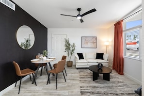 Ein modernes Wohnzimmer mit Essbereich, einer Couch, einem Couchtisch und einem Deckenventilator.
