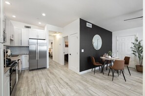 Eine moderne Küche mit einem Edelstahl-Kühlschrank, weißen Schränken und einem Essbereich mit einem runden Spiegel und braunen Stühlen.