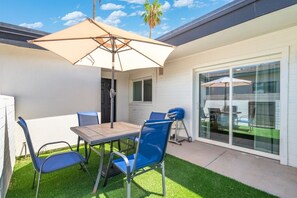 Eine Terrasse mit Tisch und Stühlen, einem Grill und einer Glasschiebetür zu einem überdachten Außenbereich.
