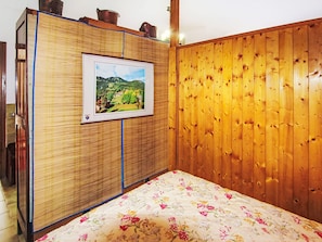 Una camera da letto con un armadio in legno, un quadro appeso al muro e una coperta con motivi floreali.