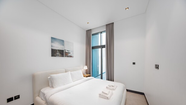 Ein Hotelzimmer mit einem großen Bett, einem Nachttisch, einer Lampe, einem Wandbild und einem Fenster mit Vorhängen.