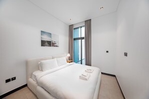 Ein Hotelzimmer mit einem großen Bett, einem Nachttisch, einer Lampe, einem Wandbild und einem Fenster mit Vorhängen.
