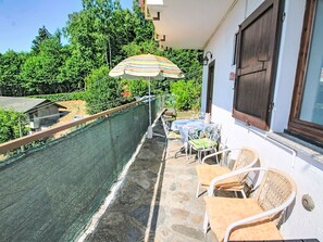 A balcony with outdoor furniture, a striped umbrella, and a view of a garden. - Apartment Susy by Interhome (Miazzina)