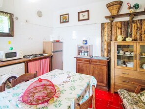 Cocina compacta con microondas, estufa y refrigerador. Hay una mesa de comedor con mantel floral y una silla roja.
