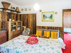 A bedroom with a wooden headboard, a bed with a floral bedspread, a wooden cabinet, and a wall-mounted shelf with decorative items. - Apartment Susy by Interhome (Miazzina)