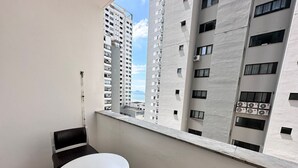 A balcony with a table and chairs, overlooking a cityscape with tall buildings and a distant view of the sea. - Just 50 meters from the beach with 2 bedrooms and parking (Balneário Camboriú)