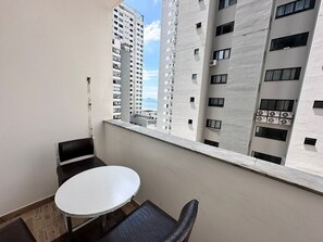 Un balcón con mesa y sillas, con vistas a un paisaje urbano de edificios altos y una vista distante del mar.