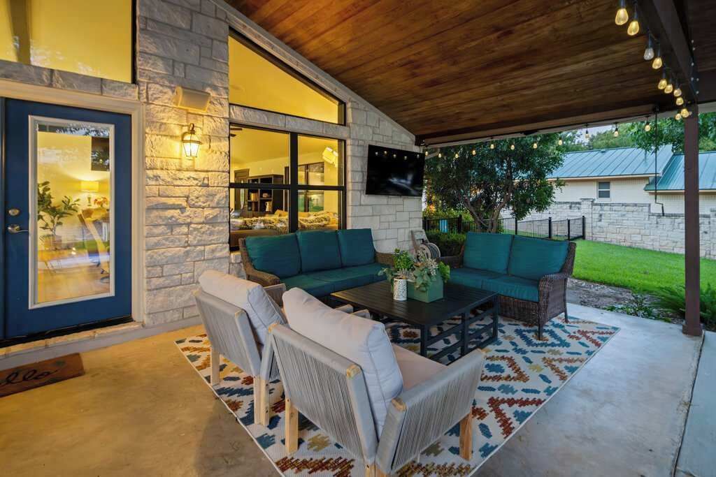 A covered patio area with a stone wall, a sofa set, a coffee table, and a television mounted on the wall.