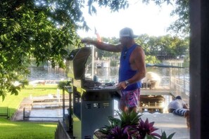 A person grilling outdoors with a view of a water body and a grassy area. - Lakeshore Retreat | Pool, Spa & Private Peninsula (Kingsland)