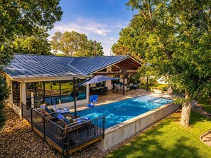 Ein Schwimmbecken mit überdachter Terrasse, Liegestühlen und einer Pergola.