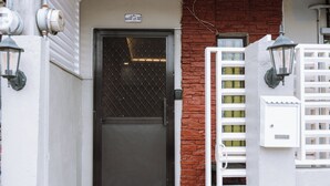 Una puerta negra con mosquitero, un buzón blanco y una pared de ladrillo.