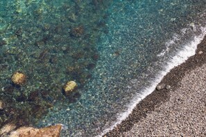 Ein Strand mit klarem Wasser, Kieselsteinen und einem Felsen.