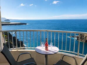 Ein Balkon mit Tisch, zwei Stühlen und einer Weinflasche.