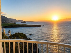 Ein Küsten-Sonnenuntergang vom Balkon mit Geländer, Blick auf das Meer und das entfernte Land.