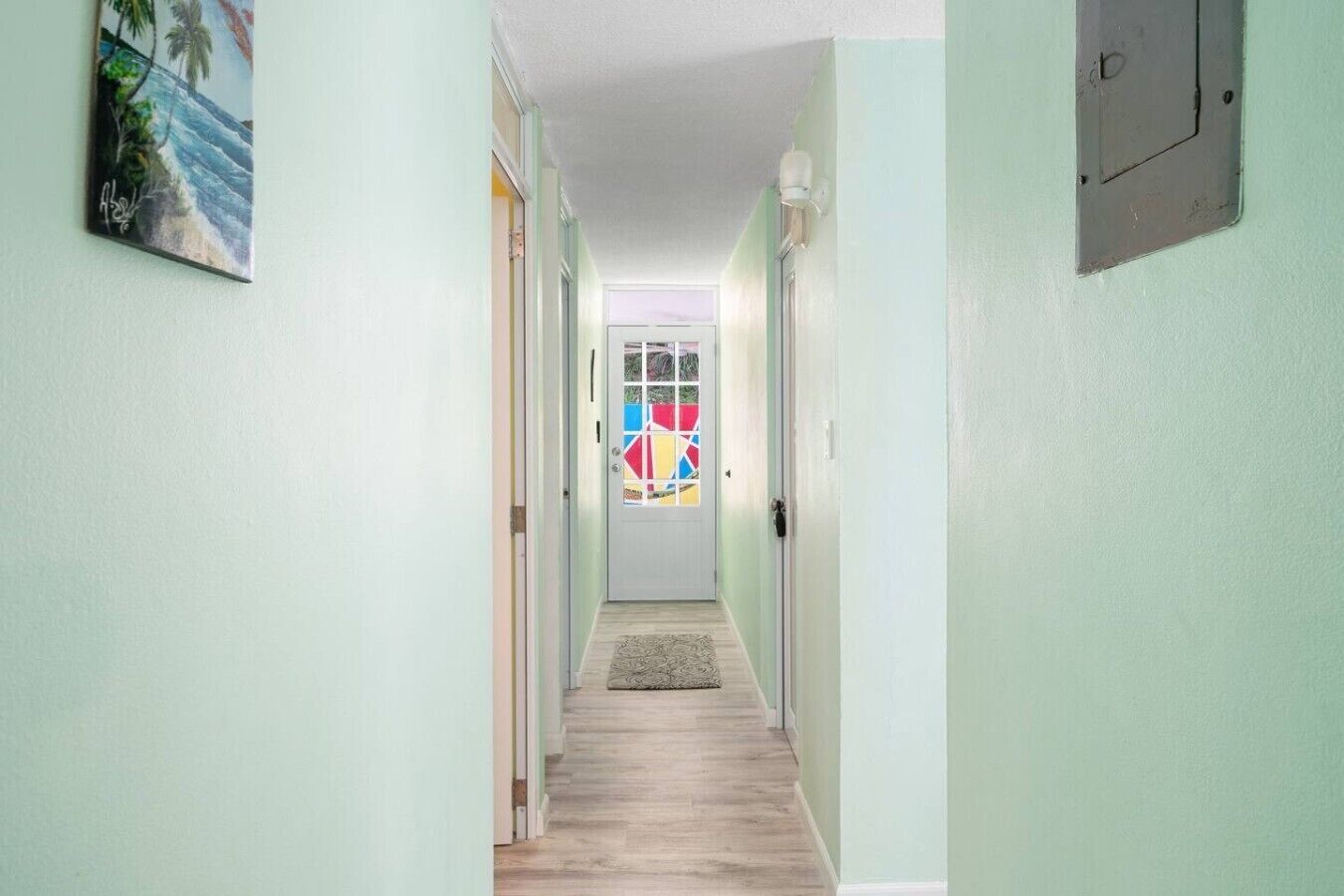 Un couloir aux murs vert clair, doté d’un plancher en bois et d’une porte ornée de motifs géométriques colorés.