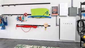 A room with a white wall, a Tesla charging station, and various items like a green paddleboard, a red paddle, and a blue kayak. - Jardines Casita - 5 min walk to downtown Rincon (Ensenada)
