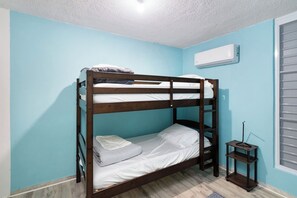 A bunk bed in a room with light blue walls, a window with blinds, and an air conditioning unit on the wall. - Jardines Casita | 5-Min Walk to Downtown Rincón (Ensenada)