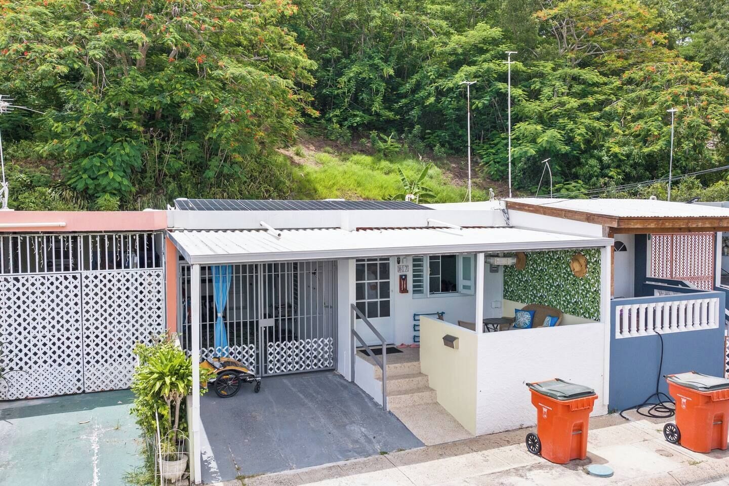 Ein Wohnhaus mit überdachtem Außenbereich, einer Treppe zu einer Veranda und einem eingezäunten Garten.