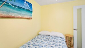 A bedroom with a bed, a stool, a door, and a wall painting of a beach scene. - Jardines Casita - 5 min walk to downtown Rincon (Ensenada)