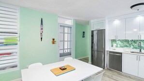 A compact kitchen with white cabinets, a stainless steel refrigerator, and a window with blinds. - Jardines Casita - 5 min walk to downtown Rincon (Ensenada)