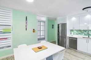 Eine kompakte Küche mit weißen Schränken, einem Edelstahlkühlschrank und einem Fenster mit Jalousien.