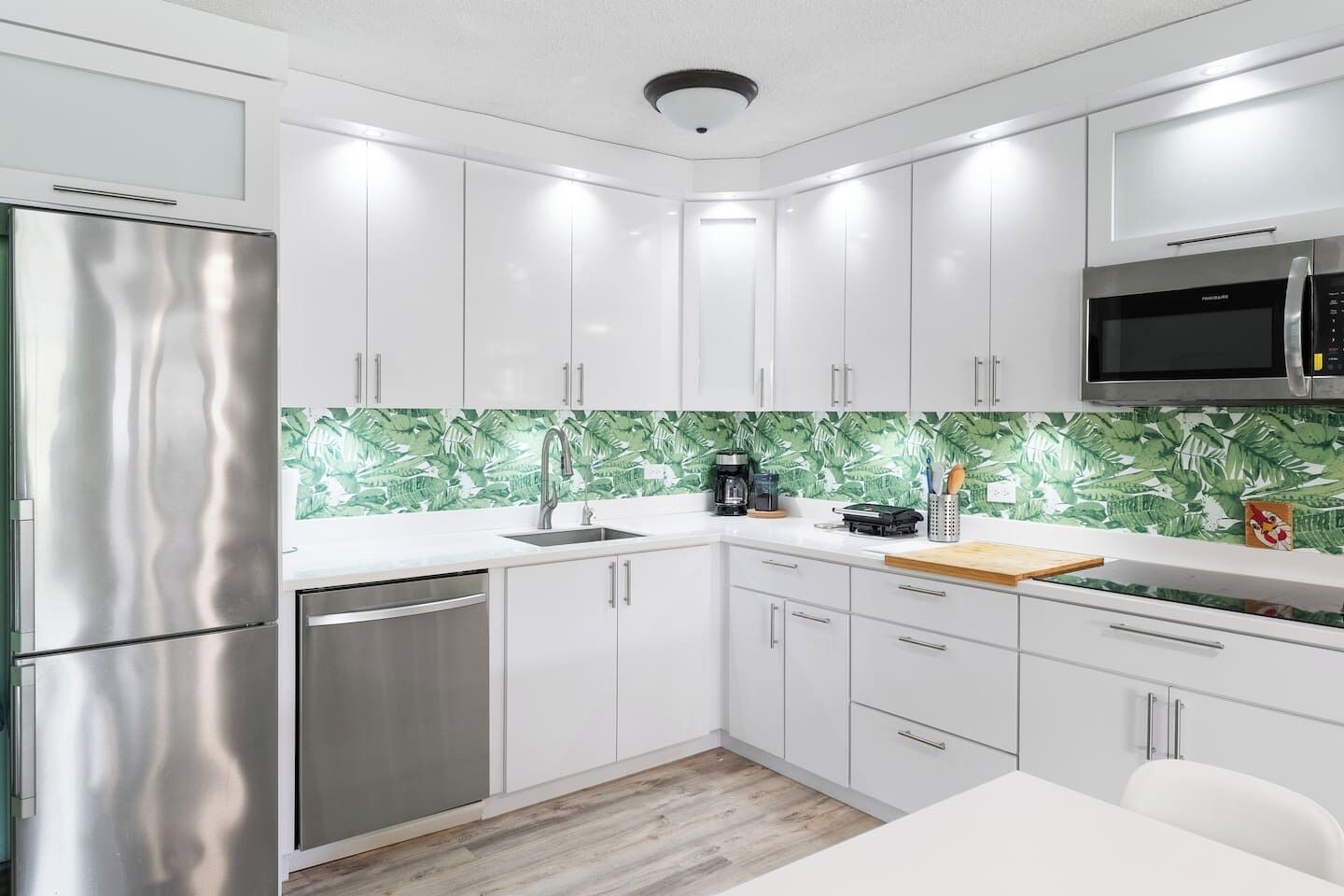 A modern kitchen with white cabinets, stainless steel appliances, and a green leaf-patterned backsplash.