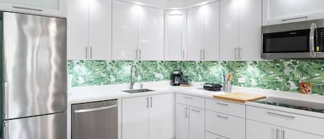 A modern kitchen with white cabinets, stainless steel appliances, and a green leaf-patterned backsplash.