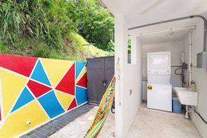 A laundry facility with a colorful wall, a washing machine, and a sink. - Jardines Casita | 5-Min Walk to Downtown Rincón (Ensenada)
