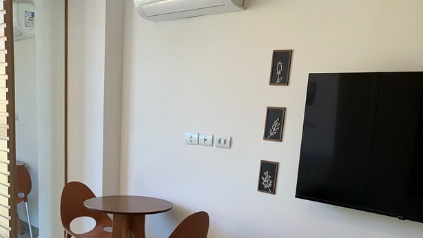 Et hotelværelse med en seng, et rundt bord med to stole, et fladskærms-TV og en vægmonteret aircondition.