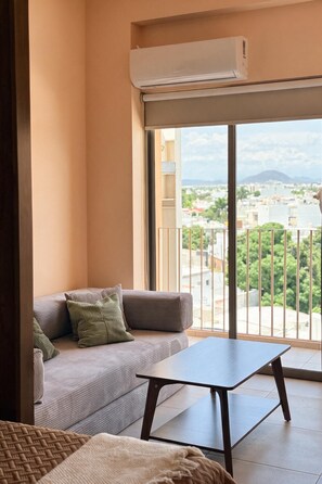 Ein Balkon mit einer Couch und einem Tisch, einer Klimaanlage und Blick auf eine Stadtlandschaft.