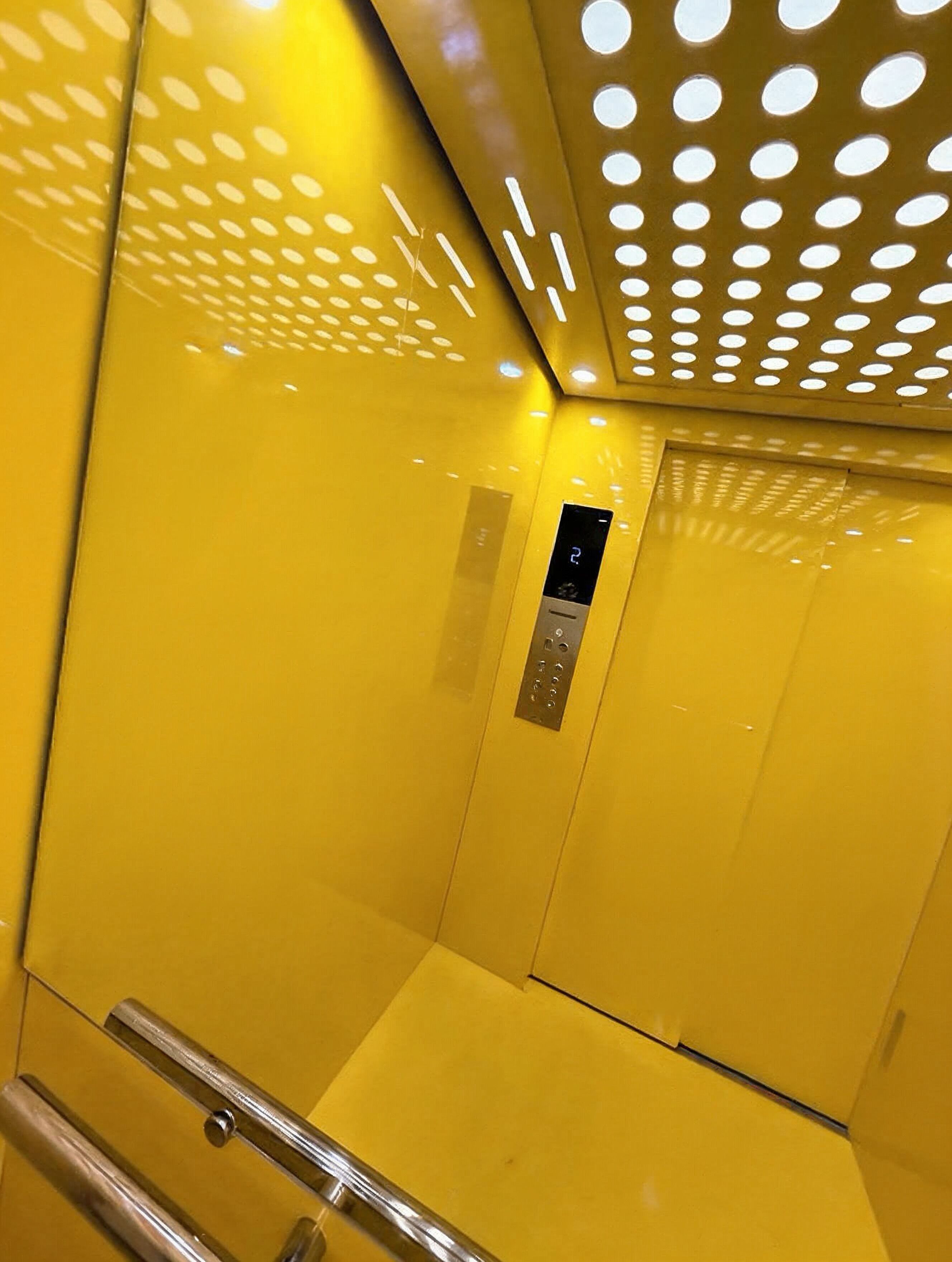 An elevator interior with a metallic control panel and reflective yellow walls.