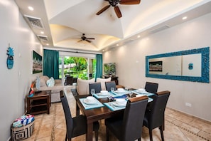 A dining area with a table set for four, a ceiling fan, and a view of a garden through a glass door. - Poolside condo, 3-min walk to Tamarindo Beach (Tamarindo)