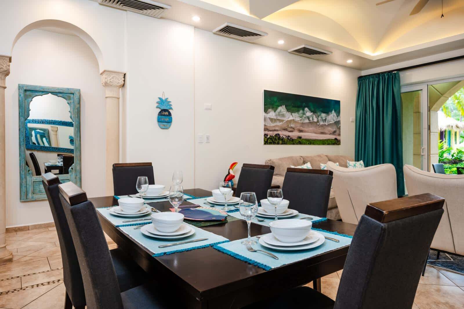 A dining area with a table set for four, chairs, and a painting on the wall.