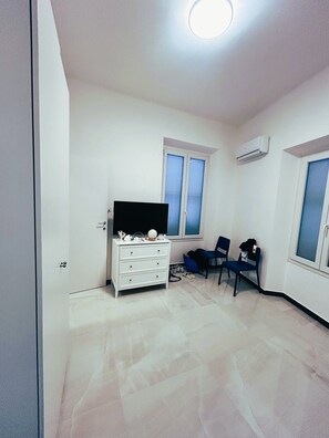 Una habitación con un tocador blanco, un televisor de pantalla plana, dos sillas y una ventana.