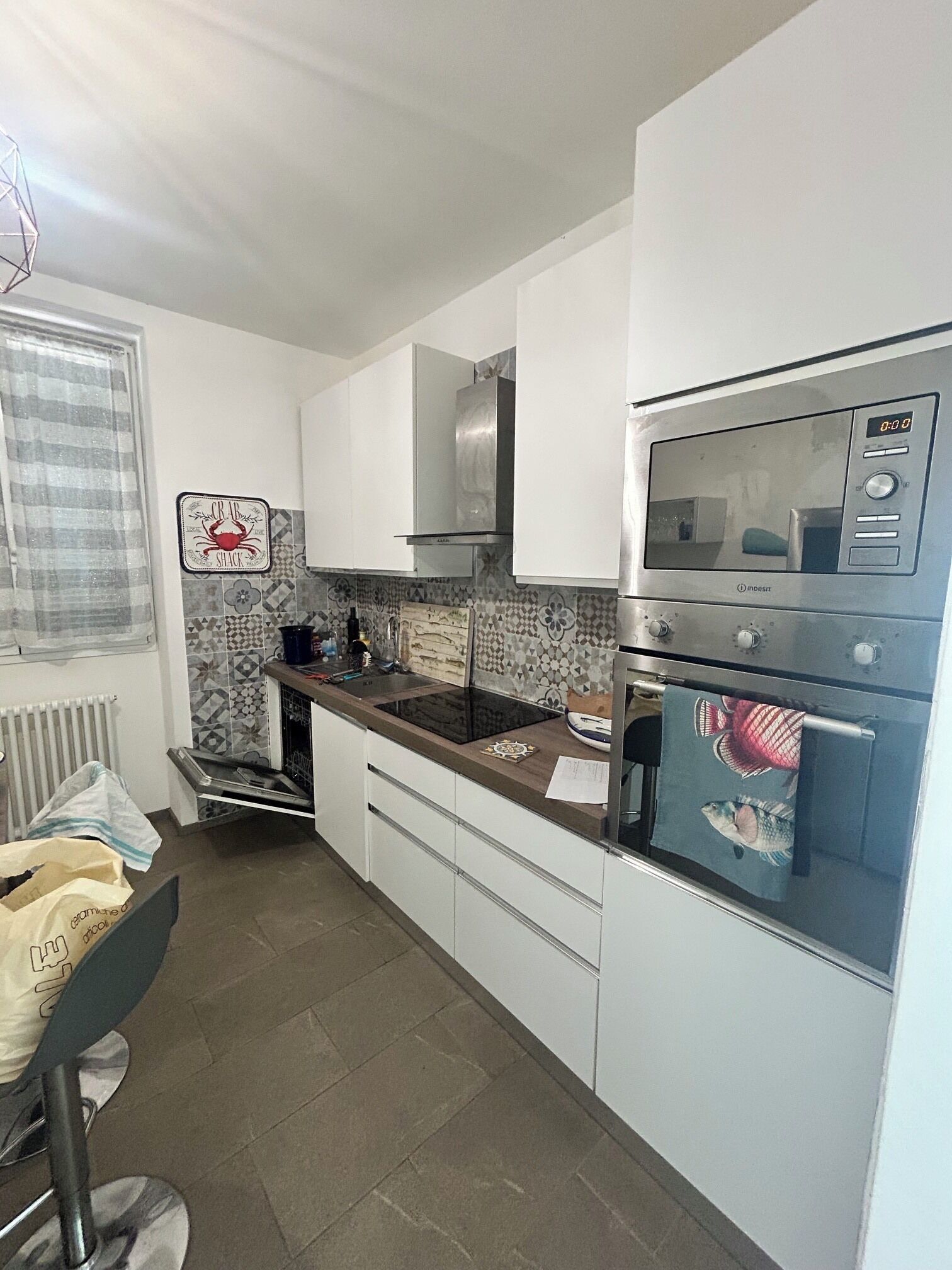 A compact kitchen with white cabinets, a stainless steel range hood, a built-in oven, and a refrigerator with a digital display.