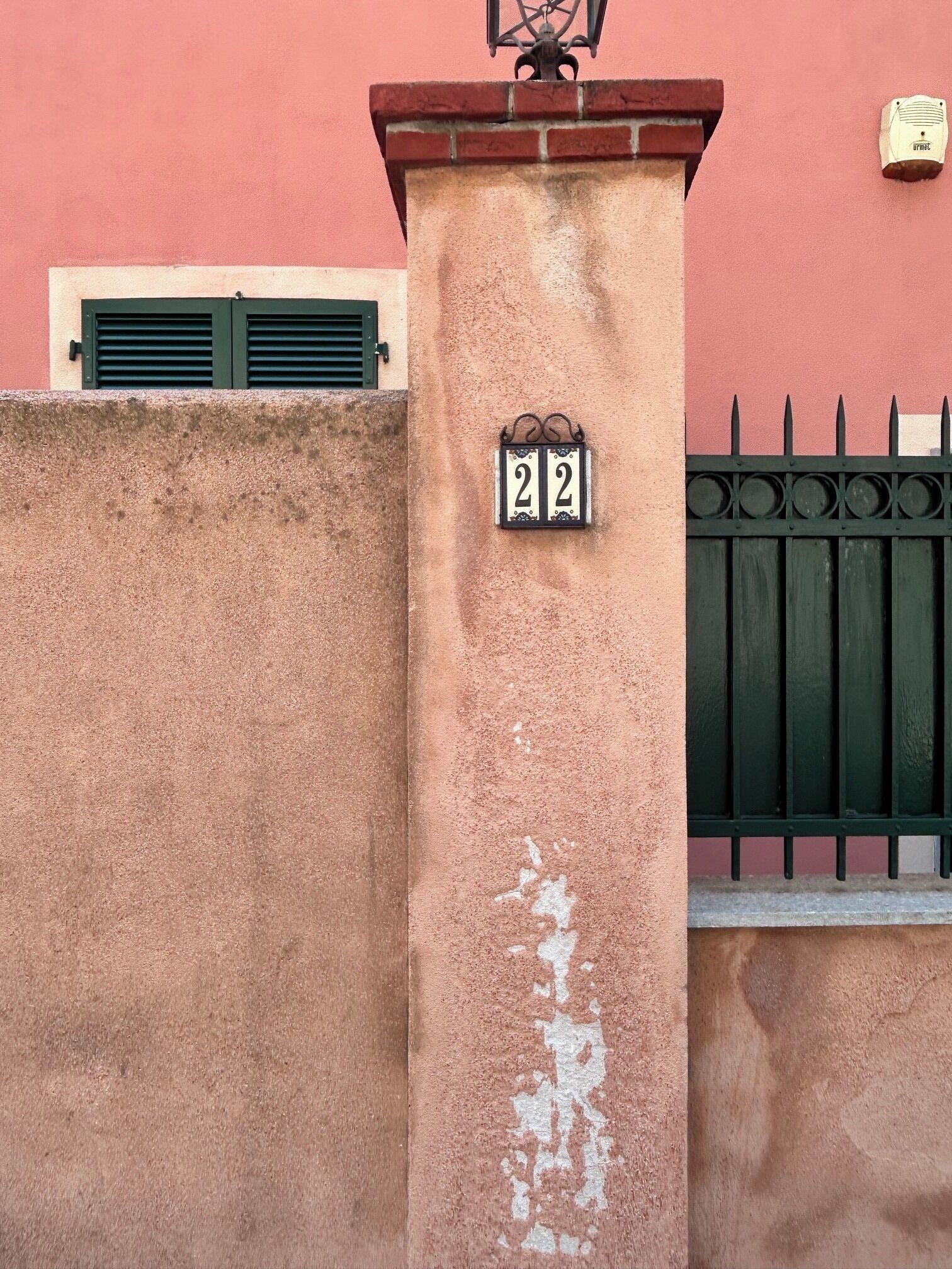 A building facade with a number plaque, a window with shutters, and a metal gate.