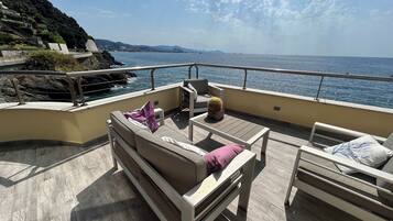 A deck with a sofa, a small table, and a chair, overlooking a body of water and a distant coastline.
