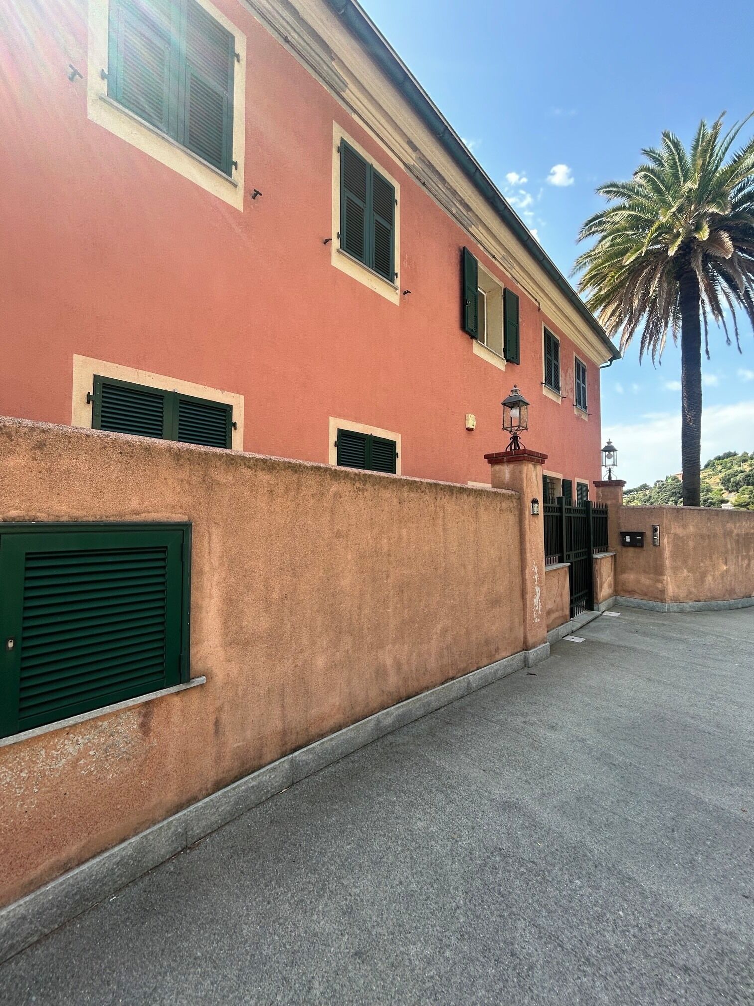 Ein Gebäude mit roter Fassade, grünen Fensterläden und einer Palme im Hintergrund.