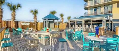 An outdoor patio area with tables and chairs, a covered seating area, and a wooden deck.
