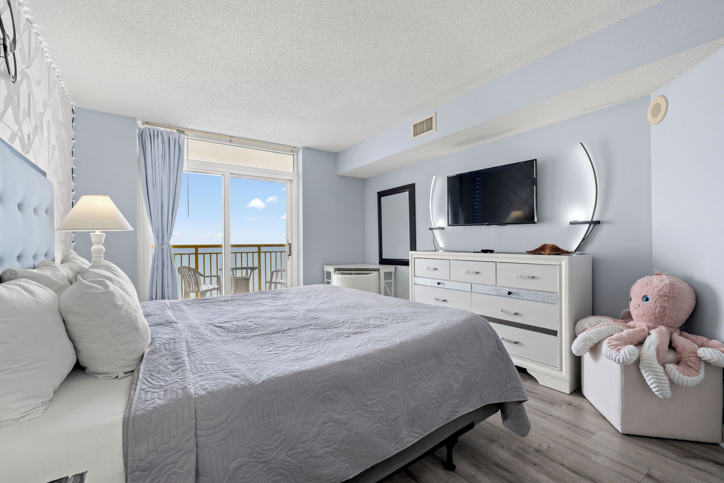 Una habitación de hotel con cama, cómoda, televisor y balcón.