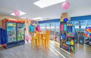 A brightly lit indoor space with a seating area, a refrigerator stocked with beverages, and shelves with various items. - Spacious 3-bedroom 3-bathroom beachfront condo in North Myrtle Beach (North Myrtle Beach)