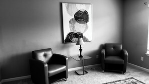 Une pièce comprenant deux fauteuils en cuir, une petite table avec une lampe et un grand tableau abstrait accroché au mur.